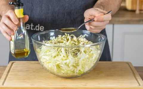 Ein Löffel Öl wird über den fein geschnittenen Spitzkohl gegeben, der für Omas Spitzkohlsalat vorbereitet wird.