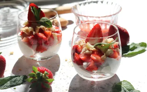 Zwei Gläser mit einem leichten Erdbeer Quark Dessert, garniert mit frischen Erdbeeren und Minze.