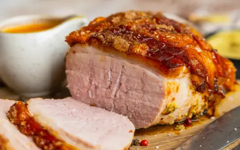 Saftiger Braten mit knuspriger Kruste, perfekt für die Zubereitung von Prager Schinken im Backofen. Dazu eine Schüssel mit Sauce.