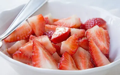 Schüssel mit marinierten Erdbeeren, die mit einem Löffel serviert werden. Saftige, rote Erdbeerstücke glänzen im Licht.