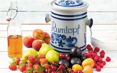 Früchte für ein Rumtopf Rezept nach Oma: Erdbeeren, Kirschen, Aprikosen, Pflaumen, Pfirsiche, Birnen, Himbeeren und eine Flasche Schnaps.