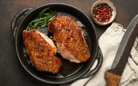 Zwei perfekt gebratene Entenbrüste in einer Pfanne, garniert mit Rosmarin und rosa Pfeffer. Ein klassisches Entenbrust Rezept, bereit zum Servieren.