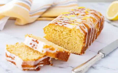 Saftiger zitronenkuchen mit Joghurt, überzogen mit Zuckerguss und garniert mit Zitronenschale. Ein Stück ist angeschnitten.