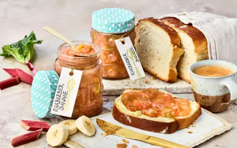 Zwei Gläser Rhabarber Bananen Marmelade, frischer Rhabarber, Bananenscheiben, Brot und Kaffee.