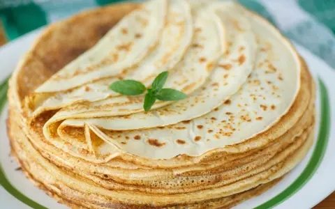Ein Stapel goldbrauner Pfannkuchen, wie nach Omas Pfannkuchen Rezept gemacht, mit einem Minzblatt garniert.