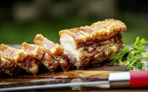 Knuspriger Schweinebauch, perfekt für ein köstliches schweinebauch rezept. Saftig, mit krosser Schwarte, auf einem Holzbrett mit Petersilie und einem Messer.