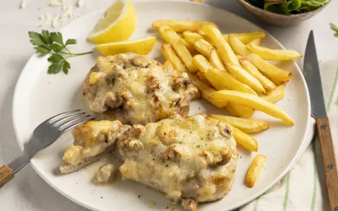 Zwei saftige Steak au Four mit geschmolzenem Käse, dazu knusprige Pommes Frites, Zitronenspalten und ein kleiner Salat.