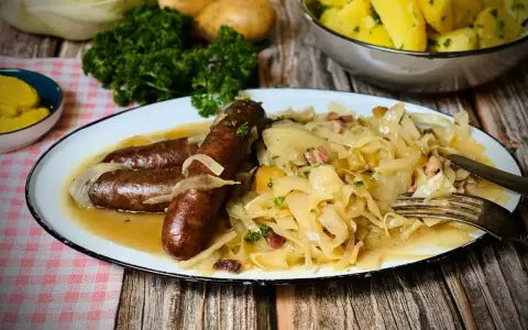 Deftige Bratwürste mit Zwiebeln auf bayrisch Kraut, garniert mit Petersilie. Dazu Salzkartoffeln und Senf.