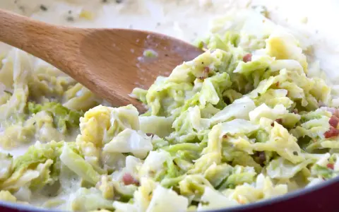 Cremiger Wirsing mit Speck, zubereitet mit einem Holzlöffel. Ein leckeres Gericht, das Lust auf mehr wirsing rezepte macht.