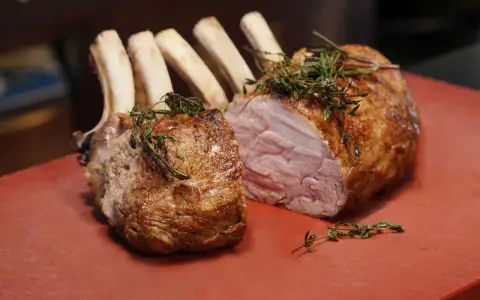 Ein gebratener Semerrolle Kalb mit Kräutern auf rotem Untergrund.
