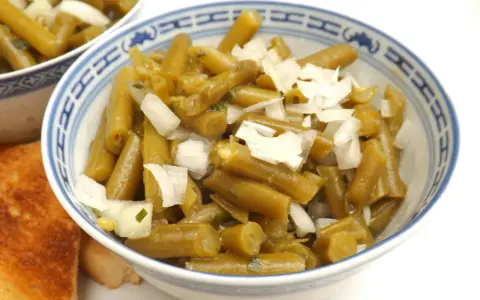 Bohnensalat rezept: Grüne Bohnen mit Zwiebeln in einer Schüssel, daneben geröstetes Brot.