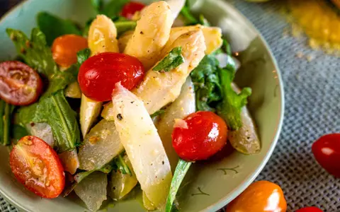 Ein Teller mit weltbestem Spargelsalat, garniert mit Kirschtomaten und frischen Kräutern. Ein Genuss für Augen und Gaumen.