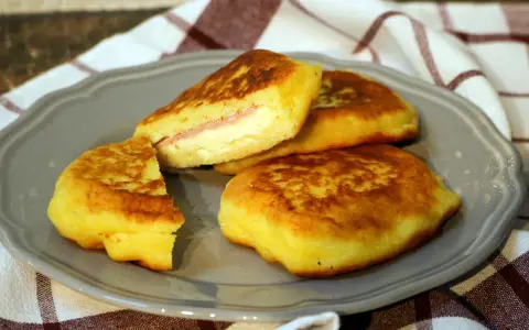 Goldbraune Kartoffel-Cordon-Bleu-Patties auf einem grauen Teller, gefüllt mit Schinken und Käse.