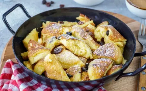 Leckerer, schneller Kaiserschmarrn im Backofen, bestäubt mit Puderzucker und Rosinen, serviert in einer Pfanne.