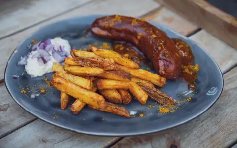 Eine saftige Currywurst im Backofen mit knusprigen Pommes und einem Klecks Mayo mit Zwiebeln.
