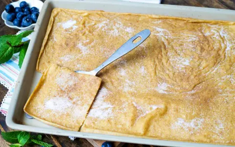 Großer, goldbrauner Ofenpfannkuchen mit Zucker und Zimt bestreut, bereit zum Servieren. Blaubeeren und Minze garnieren.