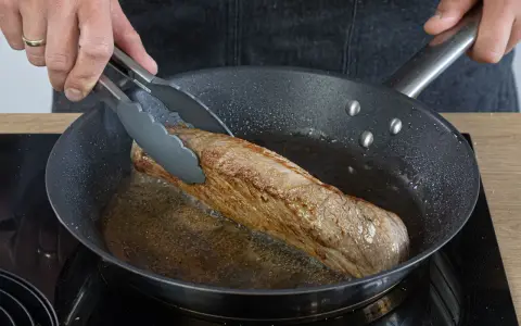 Ein saftiges Schweinefilet brät in der Pfanne. Einfache Rezepte für zartes Fleisch in der Pfanne gelingen so.