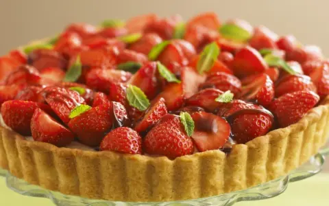 Ein köstlicher Erdbeerkuchen ohne Pudding, üppig belegt mit frischen Erdbeeren und Minze, auf einem Tortenständer.