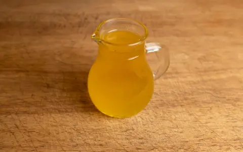Ein kleines Glas mit goldgelbem Butterschmalz steht auf einem Holzbrett. Perfekt zum butterschmalz selber machen.