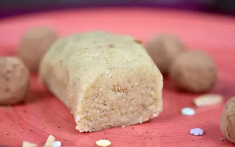 Ein Block selbstgemachtes Marzipan, ohne Rosenwasser, liegt auf einer roten Platte. Daneben sind Pralinen und bunte Zuckerstreusel.