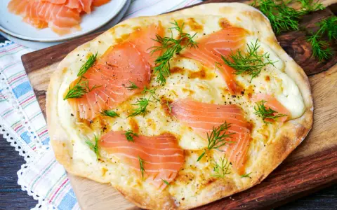 Flammkuchen mit Lachs, belegt mit zarten Lachsscheiben und frischem Dill, auf einem Holzbrett serviert.