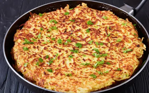 Goldbraune Kartoffel-Rösti in einer Pfanne, garniert mit Petersilie. Ein einfaches und leckeres schales Rezept für jeden Tag.