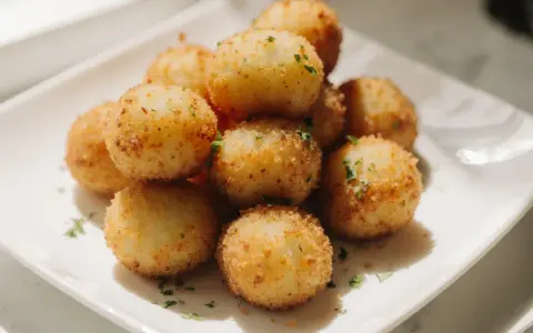 Goldbraune, knusprige kroketten aus kartoffelbrei, garniert mit Petersilie, auf einem weißen Teller.