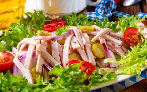 Ein leckerer Wurstsalat mit Gurken, Tomaten und Zwiebeln, garniert mit Salat. Perfekt für ein deftiges wurstsalat rezept.