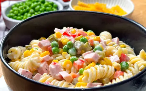 Ein cremiger nudelsalat mit mayonaise, garniert mit Erbsen, Mais, Paprika und Schinkenwürfeln.