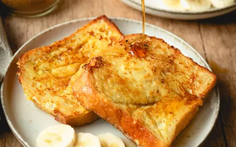 Armer Ritter, goldbraun gebraten, mit Sirup übergossen und Bananenscheiben garniert. Ein köstliches Frühstück!