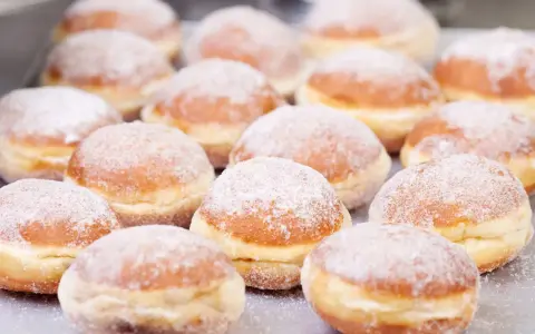 Eine Reihe von frisch gebackenen, mit Puderzucker bestäubten Berliner Pfannkuchen liegt auf einem Blech.