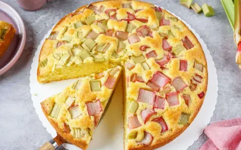 Saftiger Rhabarberkuchen, ein Klassiker unter den Rezepten mit Rhabarber. Ein Stück wird gerade herausgehoben.