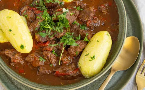 Herzhaftes Gulasch im Schnellkochtopf, serviert mit Salzkartoffeln und frischer Petersilie. Ein Klassiker, der schnell zubereitet ist.