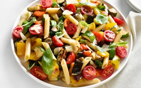 Bunter Nudelsalat ohne Mayo mit Penne, gegrilltem Gemüse, Kirschtomaten und Basilikum, garniert mit Parmesan.