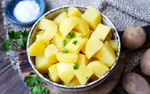 Schüssel mit dampfenden Salzkartoffeln, garniert mit Petersilie. Daneben eine kleine Schale mit Salz und rohe Kartoffeln.