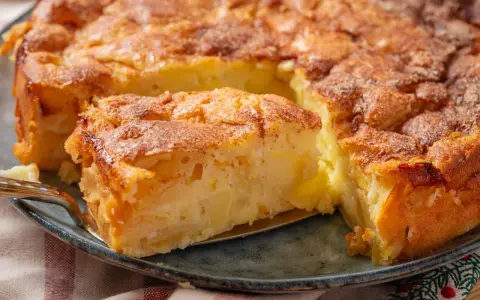 Ein Stück von einem goldbraunen, sehr feinen Apfelkuchen mit Zimt bestreut, wird mit einer Tortenheber herausgehoben.