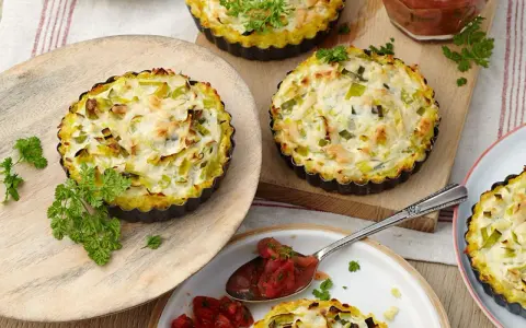 Kleine herzhafte Lauch-Tartelettes mit cremigem Belag, garniert mit Petersilie. Perfekt für Lauch Rezepte.