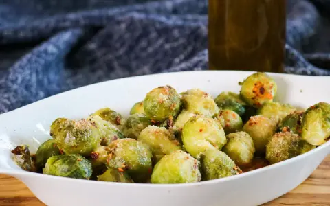 Ein weißes Ovalschälchen gefüllt mit knusprigem Rosenkohl, bestreut mit Parmesan und Chili-Flocken.