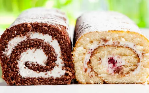 Zwei Biskuitrollen, eine schokoladig, die andere hell, mit Sahne und Fruchtfüllung, bestäubt mit Puderzucker. Wie von Landfrauen gebacken.
