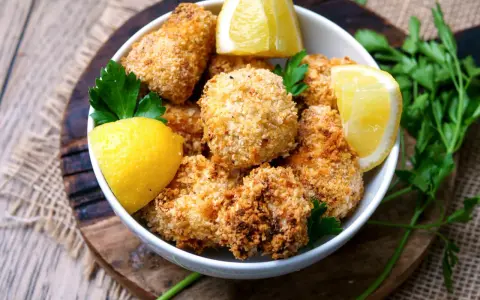 Knuspriger blumenkohl im airfryer, goldbraun paniert, serviert mit frischen Zitronenspalten und Petersilie.