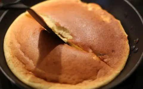 Ein goldbrauner Kaiserschmarrn wird in der Pfanne mit einem Messer zerteilt. Das perfekte Rezept für diesen Klassiker!