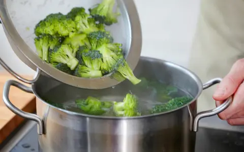 Frischer Brokkoli wird aus einem Sieb in einen Topf mit kochendem Wasser gegeben. Perfekt für eine gesunde Brokkoli-Pfanne.