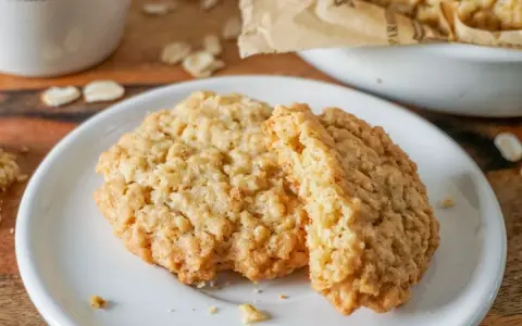 Zwei goldbraune Haferkekse liegen auf einem weißen Teller. Ein leckeres haferkekse rezept zum Nachbacken.
