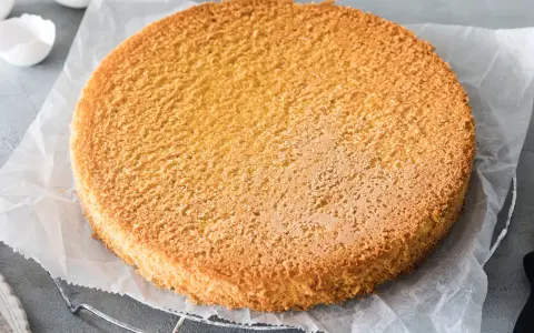 Ein goldbrauner, luftiger Biskuitboden auf Backpapier, bereit für ein köstliches Biskuitboden Rezept.
