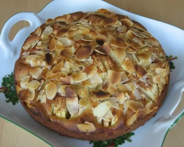Ein köstlicher, kleiner Apfelkuchen mit gerösteten Mandelblättchen auf einer verzierten Servierplatte.
