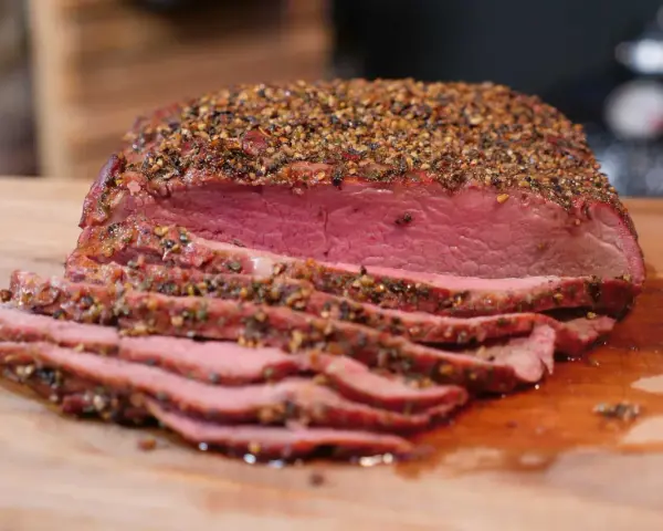 Perfekt gegarter Roastbeef Braten, saftig und rosa, mit einer würzigen Kruste aus Pfeffer und Kräutern, auf einem Holzbrett.