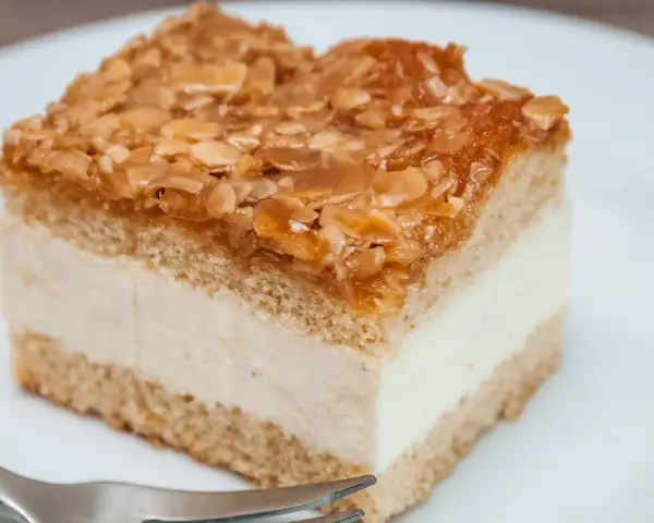 Ein Stück Bienenstich-Kuchen mit cremiger Füllung und karamellisierten Mandeln. Perfekt für das Bienenstich Rezept!