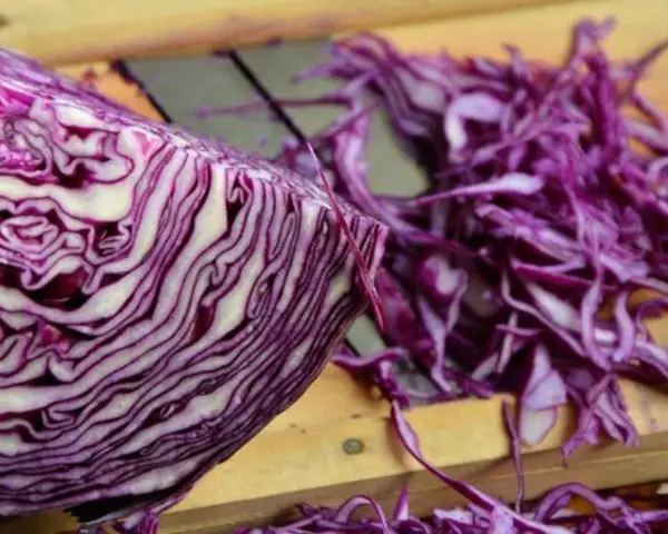 Ein halber Rotkohl liegt auf einem Holzbrett, daneben fein geschnittener Rotkohl für einen Salat.