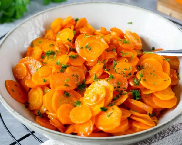 Schüssel mit glasierten Karottenscheiben, garniert mit Petersilie. Perfekt gekochte Karotten, die Lust auf mehr machen.