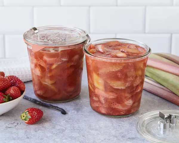 Zwei Gläser mit leckerem Rhabarberkompott, daneben frische Erdbeeren und Rhabarberstangen.